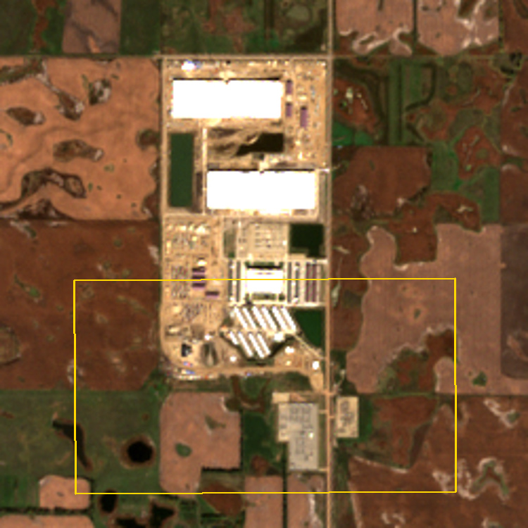 Satellite view of three large white data-center roofs north of rows of older hosting buildings and two substations on farmland west of Ellendale, North Dakota